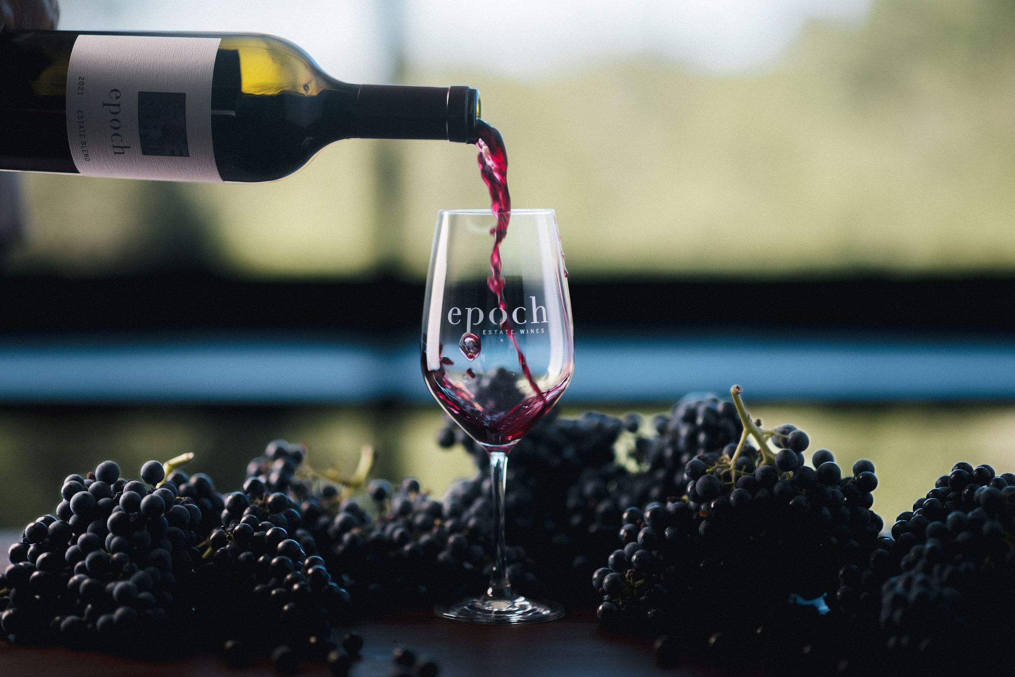 Bottle of Epoch wine being poured inot a glass surrounded by grapes